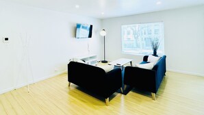 A modern living room with a black sofa, a blue sofa, a coffee table, a floor lamp, and a TV mounted on the wall. - 1BR Apt in Culver City by Just Bring Your Toothbrush (Culver City)