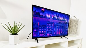 A flat-screen TV on a white entertainment unit with a cityscape wallpaper, a small potted plant, and a textured storage box. - 1BR Apt in Culver City by Just Bring Your Toothbrush (Culver City)