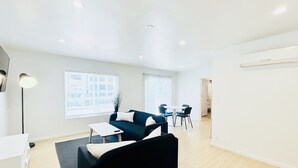 A modern living room with a black sofa, a white coffee table, and a dining area with a table and chairs. - 1BR Apt in Culver City by Just Bring Your Toothbrush (Culver City)