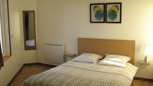 Quarto de hotel com cama, mesa de cabeceira com abajur, radiador, espelho e duas imagens de borboletas emolduradas na parede.