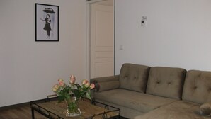 Uma sala de estar com um sofá bege, uma mesa de centro de madeira com um vaso de flores e um quadro na parede.