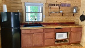 Eine kleine Küche mit einem schwarzen Kühlschrank, einem Spülbecken, einer Mikrowelle und Holzschränken.