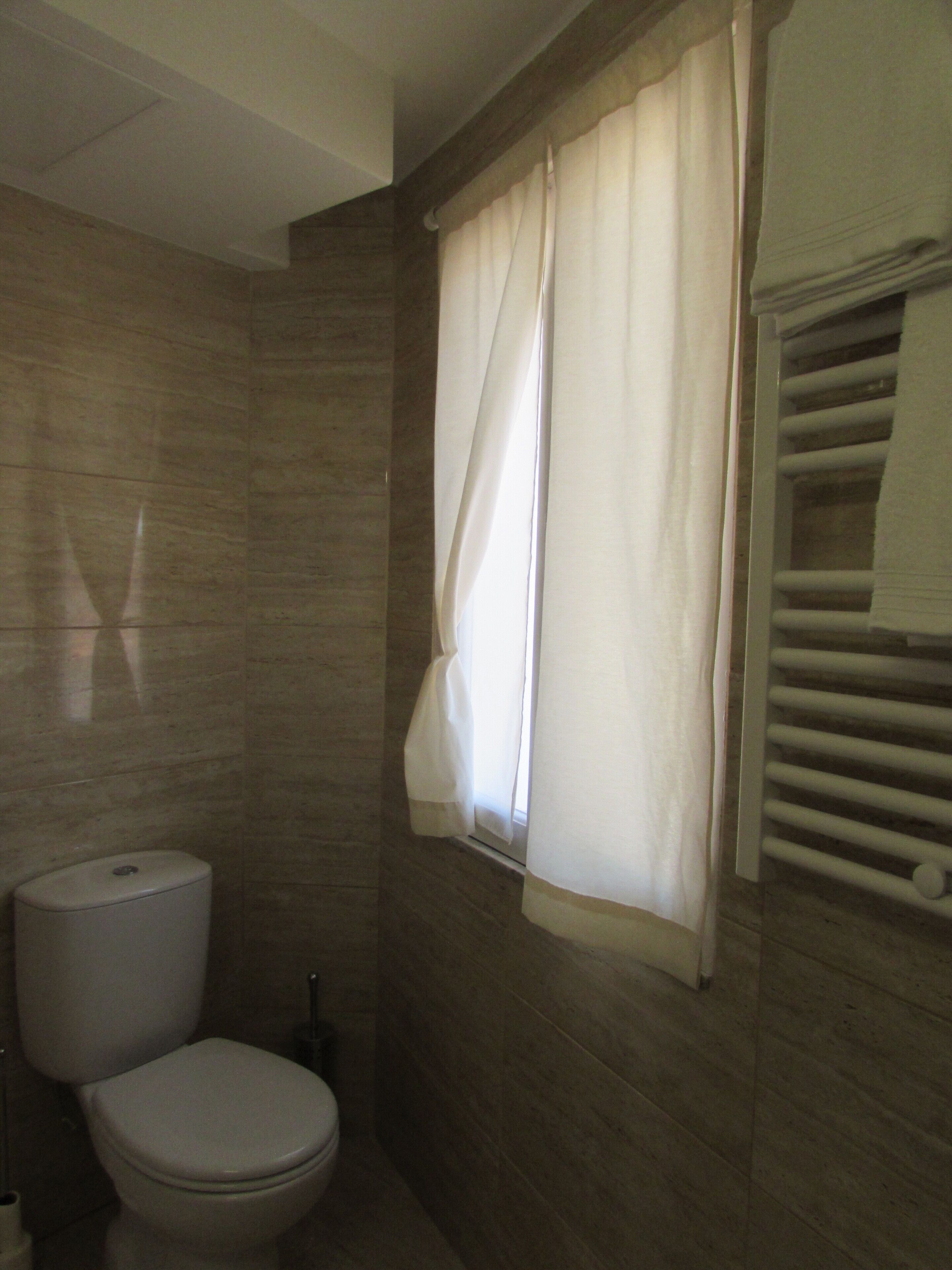 A bathroom with a toilet, a towel rack, and a window with curtains.