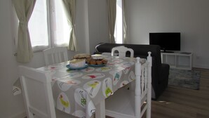 A dining area with a table set for two, a sofa, and a television in the background. - Mansão do Mé-mé - Apartamento Zêzere (Manteigas)