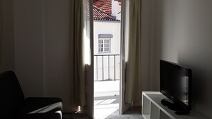 A living room with a TV on a stand, a chair, a rug, and a view through an open door to the outside. - Mansão do Mé-mé - Apartamento Zêzere (Manteigas)