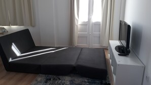 A room with a sofa bed, a television on a stand, and a window with curtains. - Mansão do Mé-mé - Apartamento Zêzere (Manteigas)