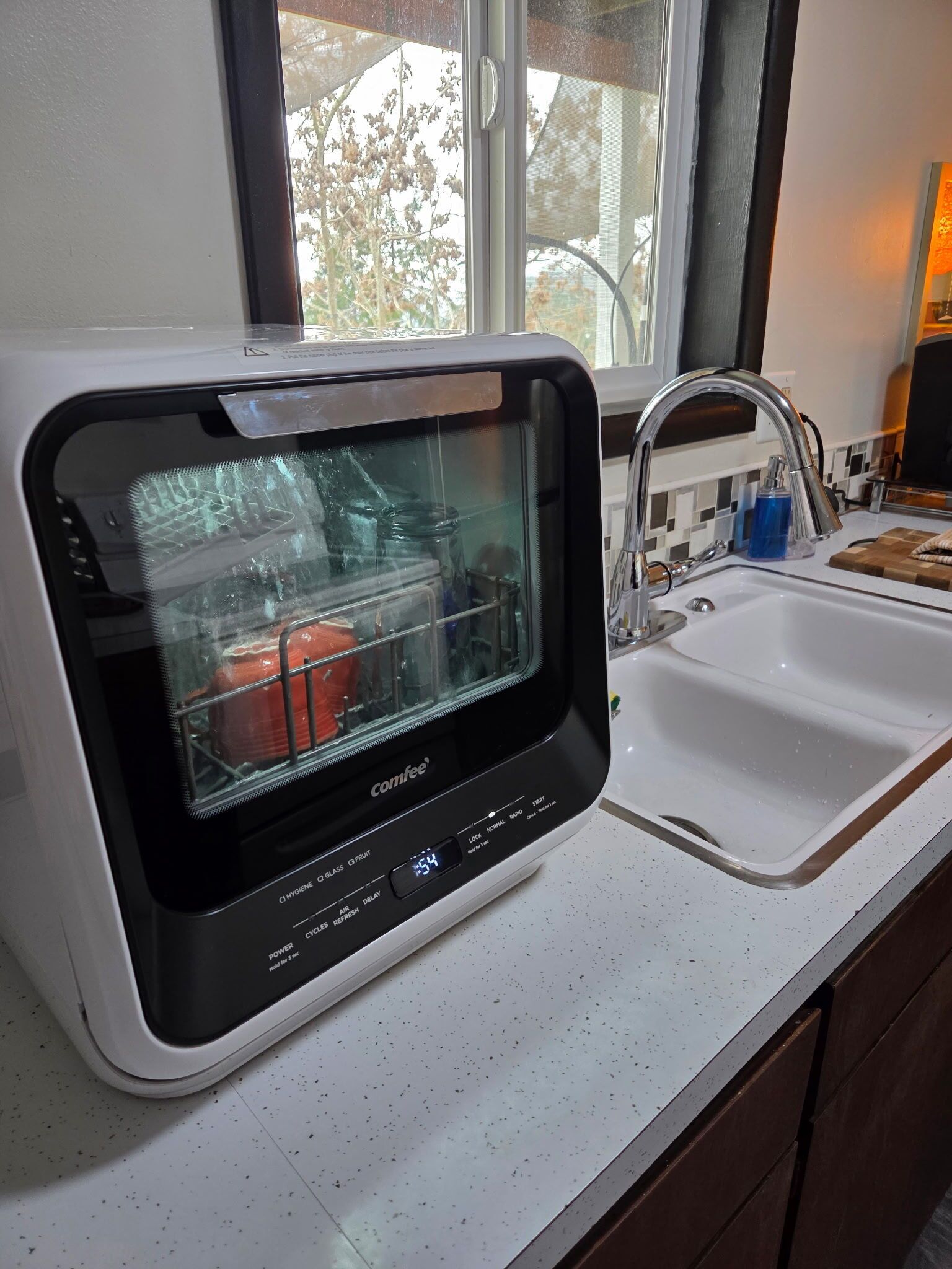 A compact kitchen with a built-in dishwasher, a sink, and a window providing natural light.