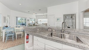 A spacious kitchen with granite countertops, a double sink, and a dining area with blue chairs.
