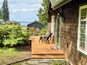 A wooden deck with outdoor furniture, a window with a green frame, and a view of a body of water. - Near Downtown Langley, Shops & Restaurants! Cozy Cottage & Pet Friendly! (Langley)