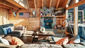 A cozy cabin interior with a fireplace, wooden walls, a sofa, and a coffee table.