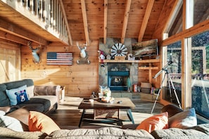 Ein gemütliches Blockhaus-Interieur mit Kamin, Holzwänden, einer Couch und einem Couchtisch.