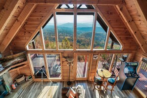 Eine Holzhütte mit einem großen Dachfenster, einem Teleskop, einem Spieltisch und einer gemütlichen Sitzecke.