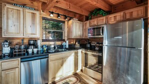 A wooden cabin kitchen with a stainless steel refrigerator, coffee maker, and wooden cabinets.