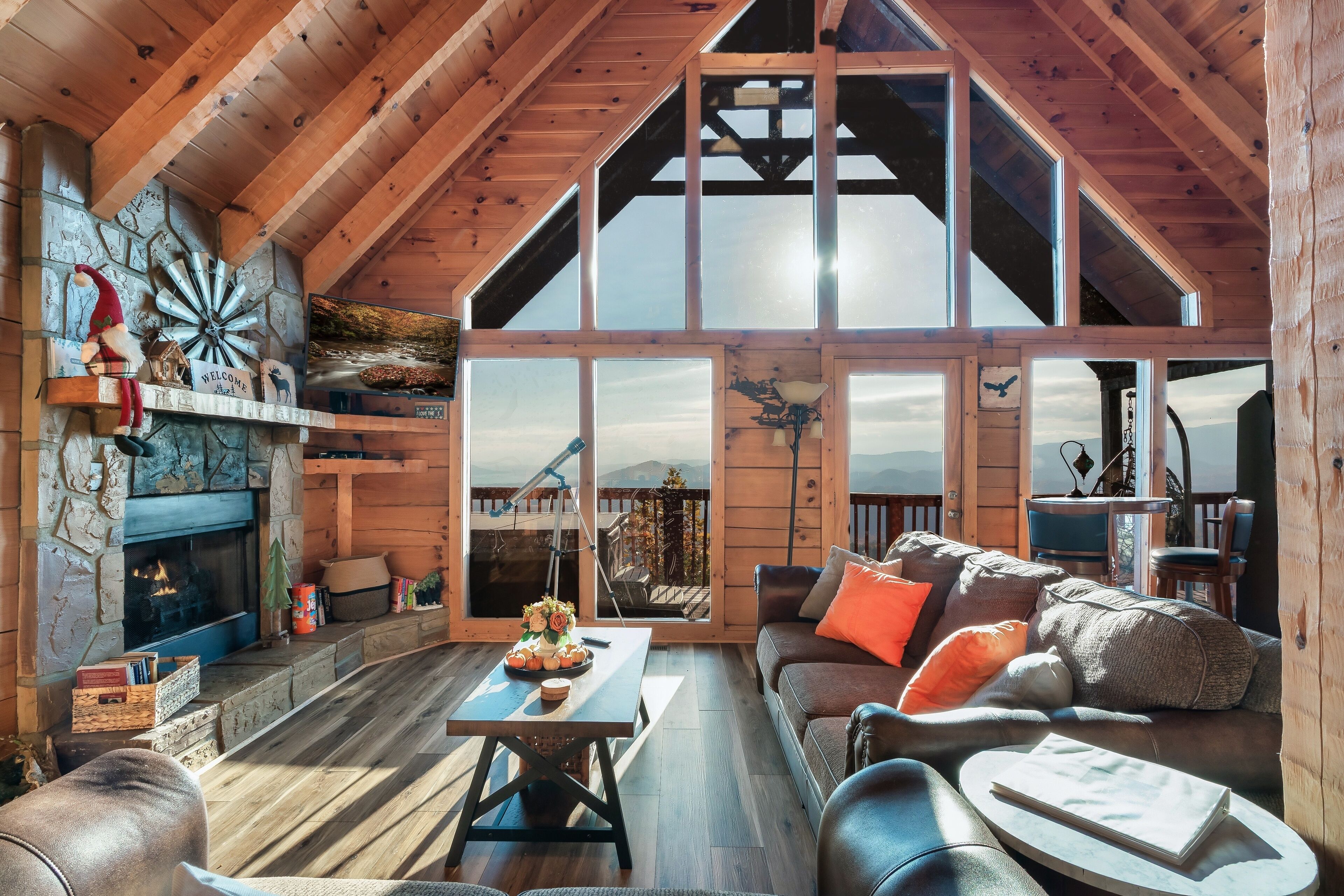 A spacious living area with a fireplace, wooden beams, a large window, and a cozy seating arrangement.