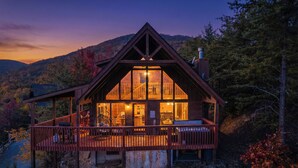 A wooden cabin with a balcony, large windows, and a chimney.
