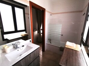 A bathroom with a white sink, a mirror, a wooden vanity, a shower with frosted glass doors, and a towel on the counter.