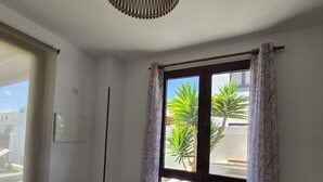 A modern dining area with a glass table and white chairs, a hanging light fixture, and a view of palm trees through a window with curtains. - Villa with private heated swimming pool, Wifi, Prime video, BBQ, tennis table (Playa Blanca)