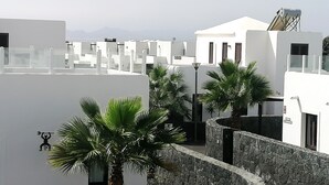 A modern building with white walls and stone accents, featuring palm trees and a clear sky. - Villa with private heated swimming pool, Wifi, Prime video, BBQ, tennis table (Playa Blanca)