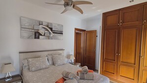 A bedroom with a bed, a ceiling fan, a wooden wardrobe, and a painting on the wall. - Villa with private heated swimming pool, Wifi, Prime video, BBQ, tennis table (Playa Blanca)