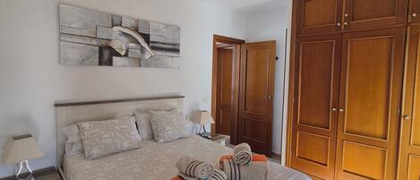 Een slaapkamer met een bed, een plafondventilator, een houten garderobe en een schilderij aan de muur.