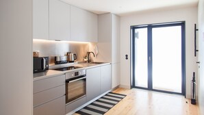 A modern kitchen with white cabinets, a built-in oven, a microwave, and a kettle.
