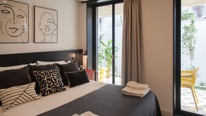 A hotel room with a large bed, multiple pillows, a nightstand with a lamp, and a view of the outdoor area through a sliding glass door.