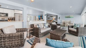 A spacious living area with wicker furniture, a ceiling fan, and a kitchen in the background. - Stunning Remodel, HEATED POOL, Brand New Furnishings, Full Canal Sunset View (Cape Coral)