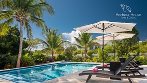 Uma piscina com espreguiçadeiras e guarda-sóis, rodeada por palmeiras e vegetação.