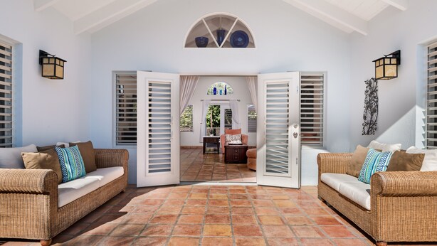 Um pátio espaçoso com dois sofás de vime, piso de azulejos e vista para uma sala de jantar através de portas abertas.