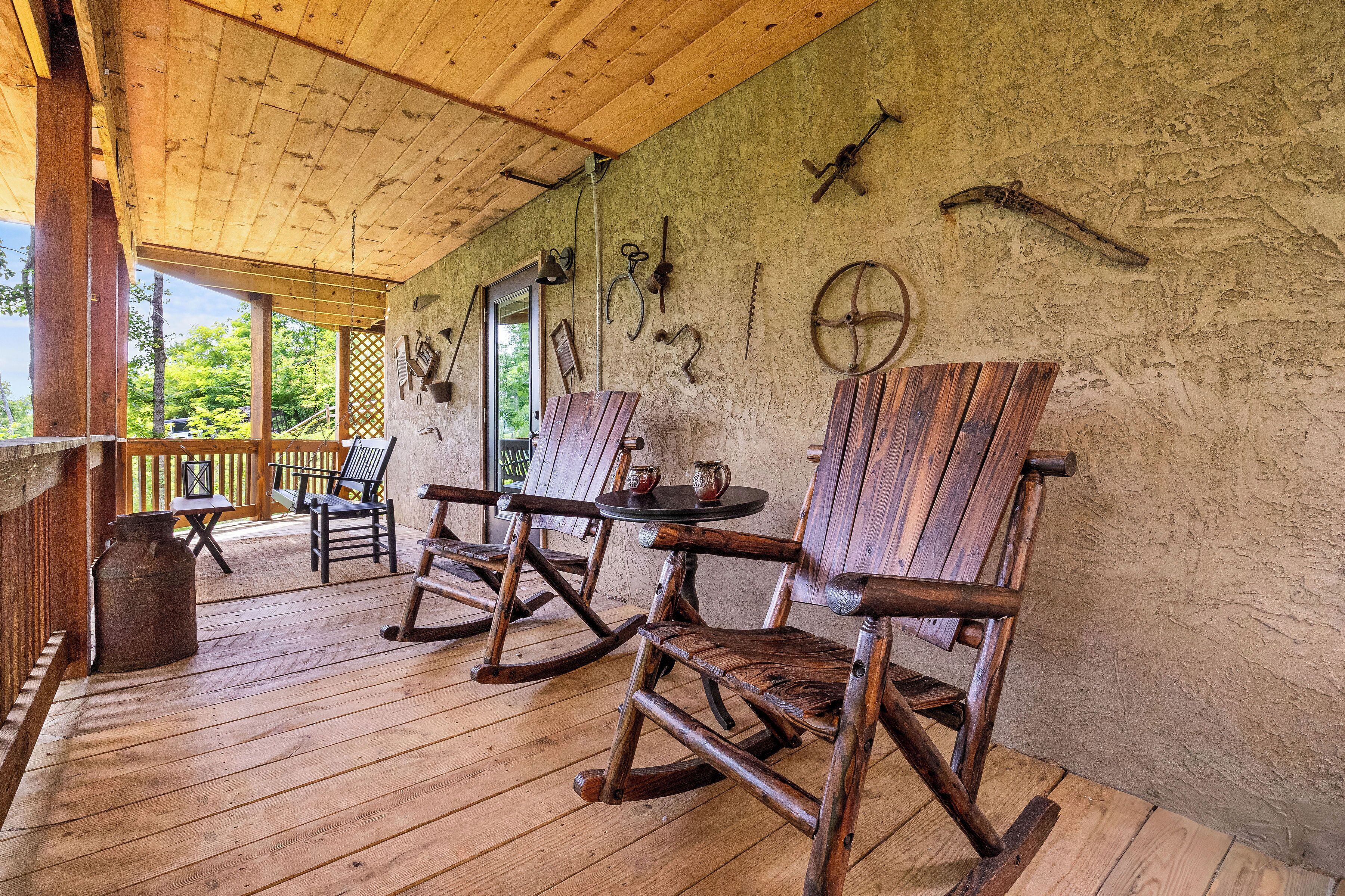 Eine hölzerne Veranda mit Schaukelstühlen und einem Tisch, rustikale Wände mit angebrachten Werkzeugen und Blick ins Grüne.