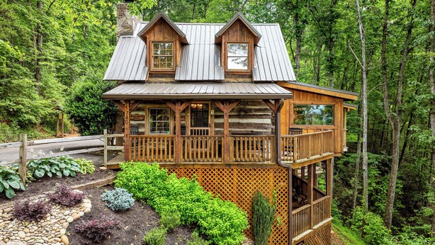 A log cabin with a balcony, surrounded by a garden with various plants and a stone pathway. - Free Tickets | Wood Burning Fireplace, Hot Tub, WIFI, Pool Table, Sleeps 7 (Gatlinburg)