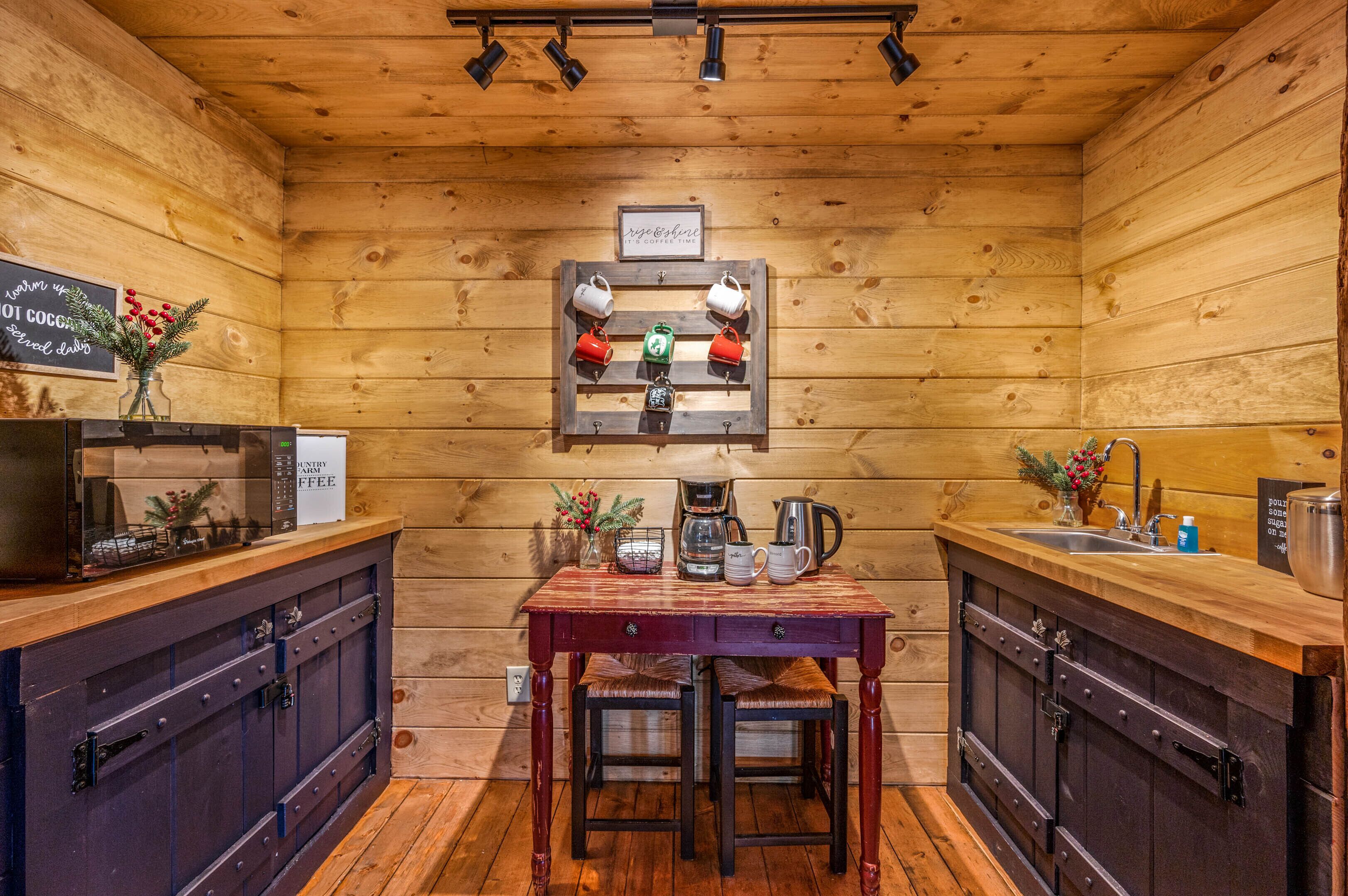 A cozy wooden cabin with a kitchen featuring a coffee station, a sink, and a dining table with chairs.