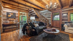 A log cabin interior with a leather sofa, a wooden coffee table, and a chandelier. - Free Tickets | Wood Burning Fireplace, Hot Tub, WIFI, Pool Table, Sleeps 7 (Gatlinburg)