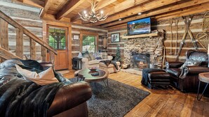 A log cabin interior with a stone fireplace, leather furniture, and a television mounted on the wall. - Free Tickets | Wood Burning Fireplace, Hot Tub, WIFI, Pool Table, Sleeps 7 (Gatlinburg)