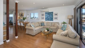 A spacious living area with a beige sofa set, a glass coffee table, and a dining area with a wooden table and chairs. - Seascape Kiama: Ocean Views, Family Fun, Pet-Friendly Perfection managed by HAUS (Kiama)