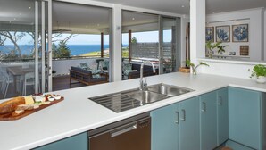 A modern kitchen with a large window, a dishwasher, and a view of the ocean. - Seascape Kiama: Ocean Views, Family Fun, Pet-Friendly Perfection managed by HAUS (Kiama)