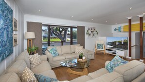 A modern living room with a beige sofa set, a glass coffee table, and a television. - Seascape Kiama: Ocean Views, Family Fun, Pet-Friendly Perfection managed by HAUS (Kiama)