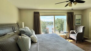 Een slaapkamer met een bed, een stoel, uitzicht op een meer en een plafondventilator.