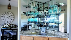 Een keuken met granieten aanrechtbladen, houten kastjes, een klok en een glazen vitrine met blauw glaswerk.