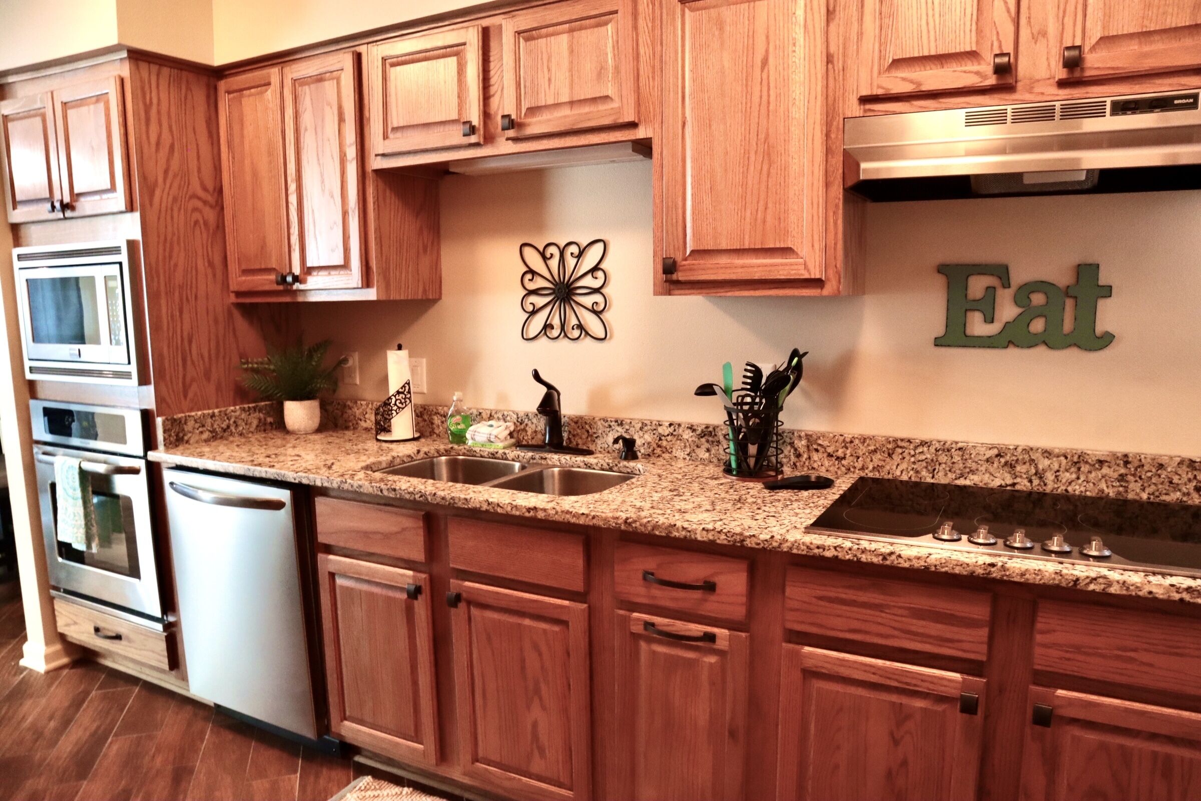 A kitchen with wooden cabinets, granite countertops, stainless steel appliances, and a decorative wall piece.