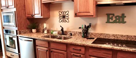 A kitchen with wooden cabinets, granite countertops, stainless steel appliances, and a decorative wall piece.