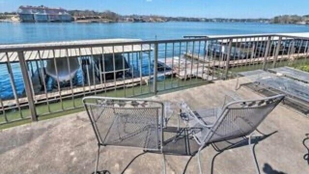Een balkon met metalen hekwerk en uitzicht op een waterpartij, met twee metalen stoelen en een betonnen vloer.