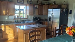 Una cocina con armarios de madera, una isla central, un refrigerador y un comedor con mesa y sillas.
