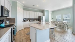 A modern kitchen with white cabinets, a central island, and a dining area with a table and chairs. - Bayfront Home with Scenic Views & Decks (Galveston)