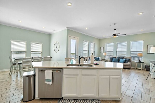 A spacious kitchen with a central island, a dining area with chairs, and a living room with a sofa and a lamp. - Bayfront Home with Scenic Views & Decks (Galveston)