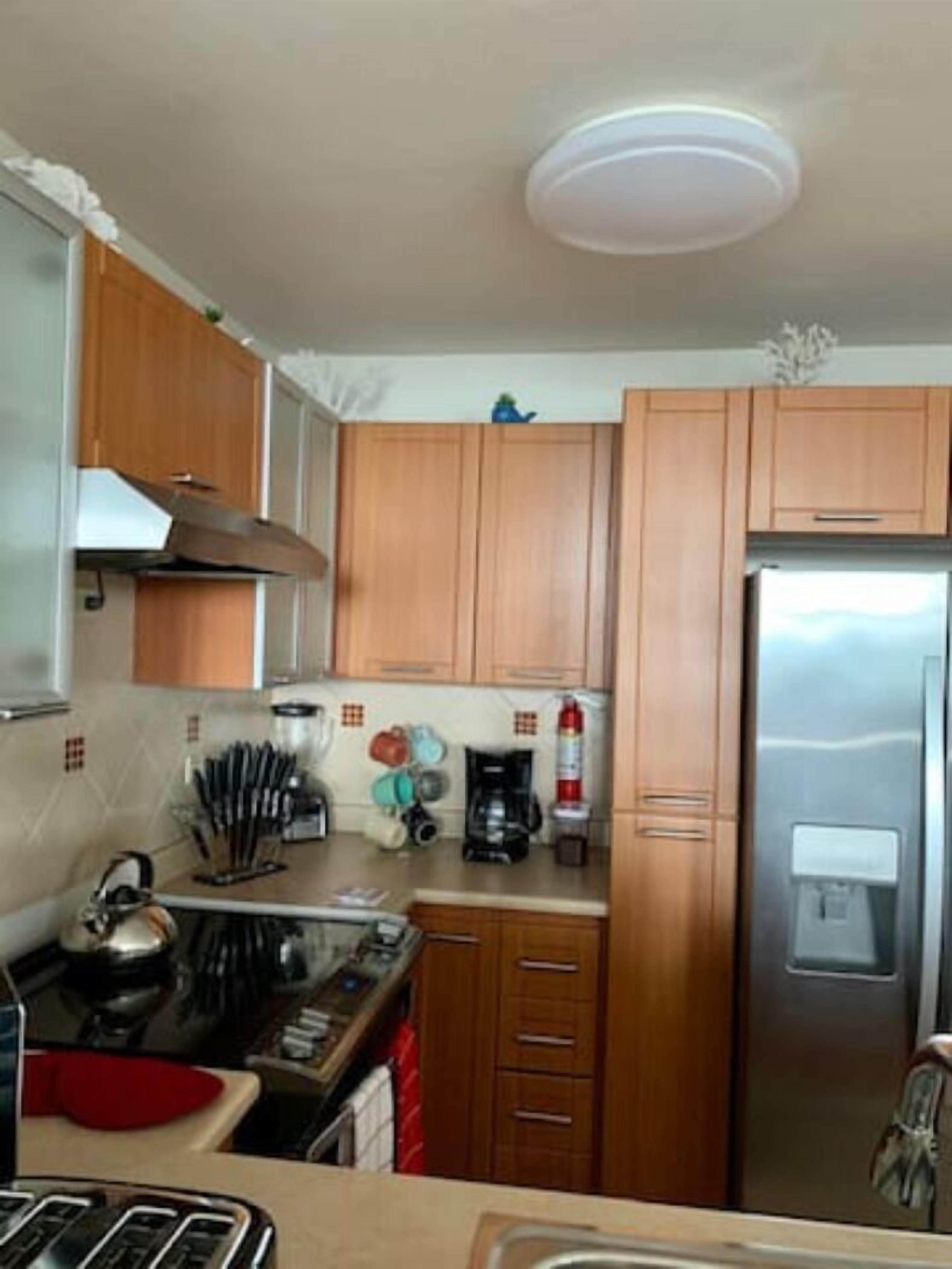 A kitchen with wooden cabinets, a stainless steel refrigerator, a stove, and various kitchen utensils.