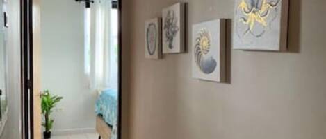 A hallway with a tiled floor, a bed with a blue cover, and several framed artworks on the wall.