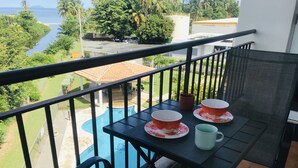Ein Balkon mit Tisch für zwei Personen, mit Blick auf einen Swimmingpool und das Meer.