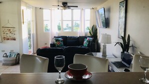 Ein Wohnzimmer mit einer Couch, einem Esstisch mit Stühlen, einem Deckenventilator und einem Fenster mit Vorhängen.