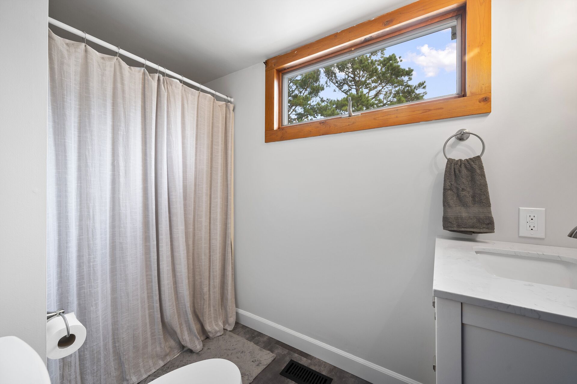 Ein Badezimmer mit Duschvorhang, Fenster, Handtuchhalter und Toilettenpapierhalter.